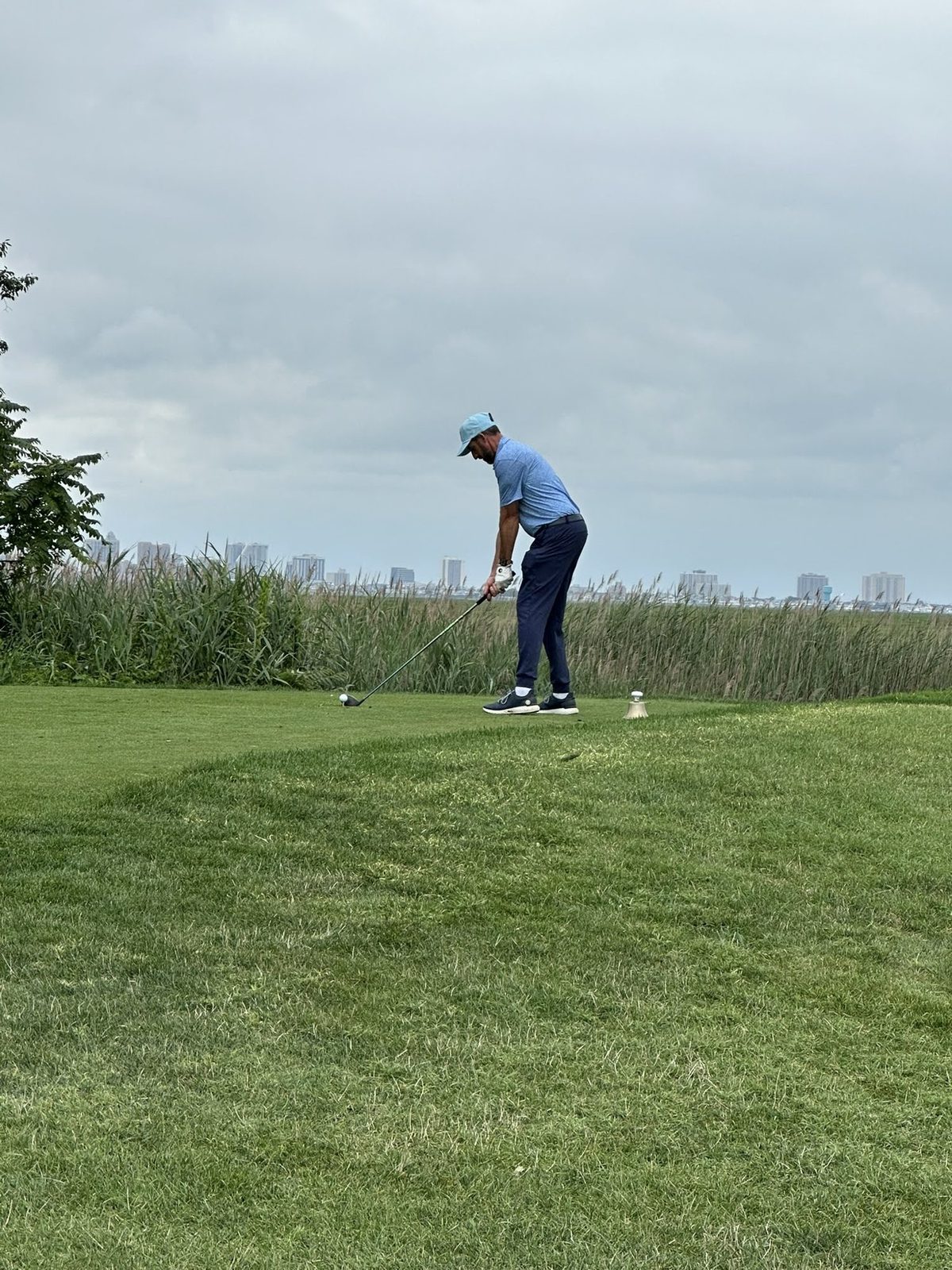 A golfer teeing off beside the marsh with the Atlantic City skyline behind